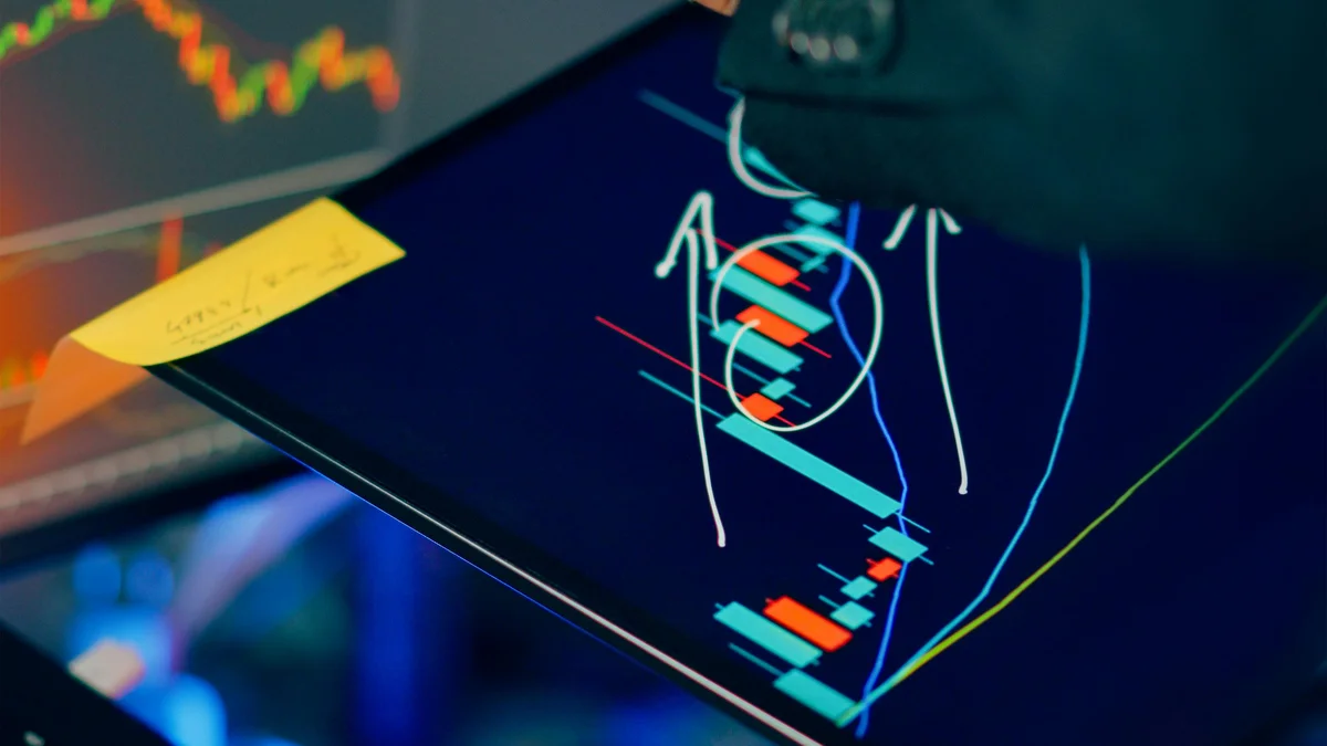 Analista financeiro examina graficos de investimento em tablet e monitor, contexto de rodada bilionaria da Anthropic