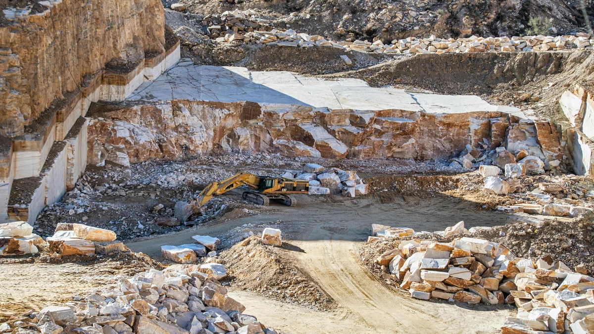 Escavadeira operando em pedreira de rocha com terreno rugoso representando mineracao de minerais estrategicos