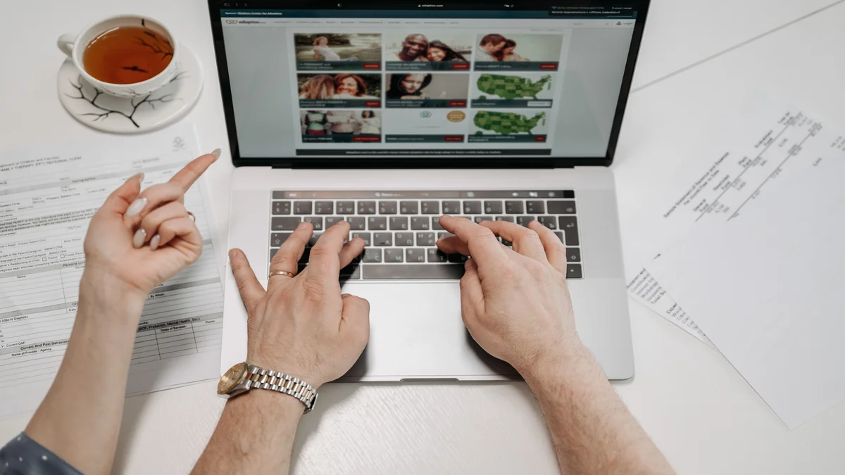 Maos digitando em laptop com documentos e processos sobre a mesa, representando advogado redigindo peticao com apoio de ferramenta de IA