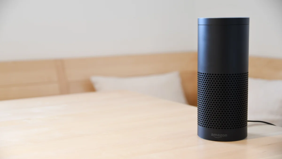 Caixa de som Amazon Echo preta sobre mesa de madeira, dispositivo compatível com a nova Alexa+