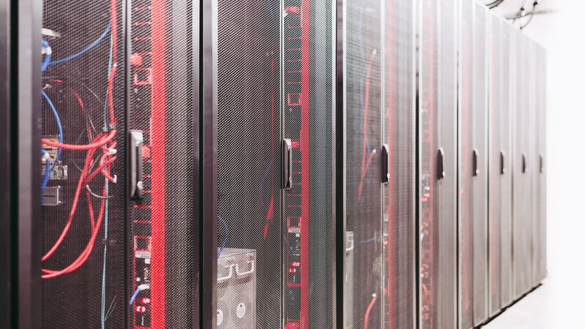 Corredor de data center com racks de servidores e cabos de rede, representando a infraestrutura de TPUs por tras de modelos de IA