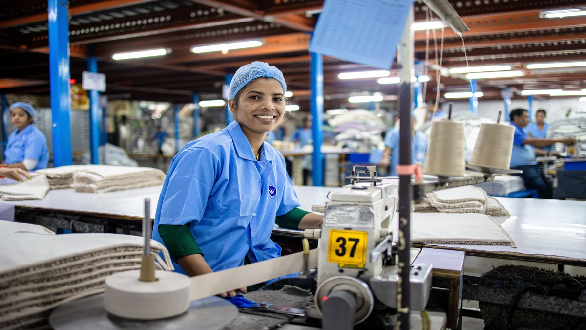 Trabalhadora sorrindo em maquina de costura em fabrica moderna