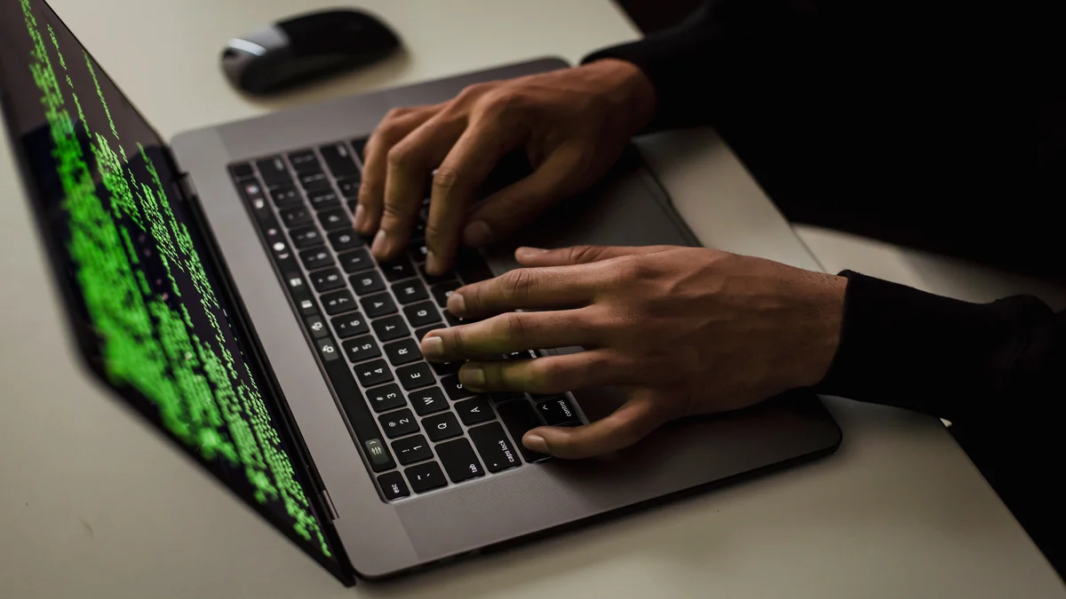 Maos digitando codigo em laptop com tela verde, representando ataque de phishing e golpe digital