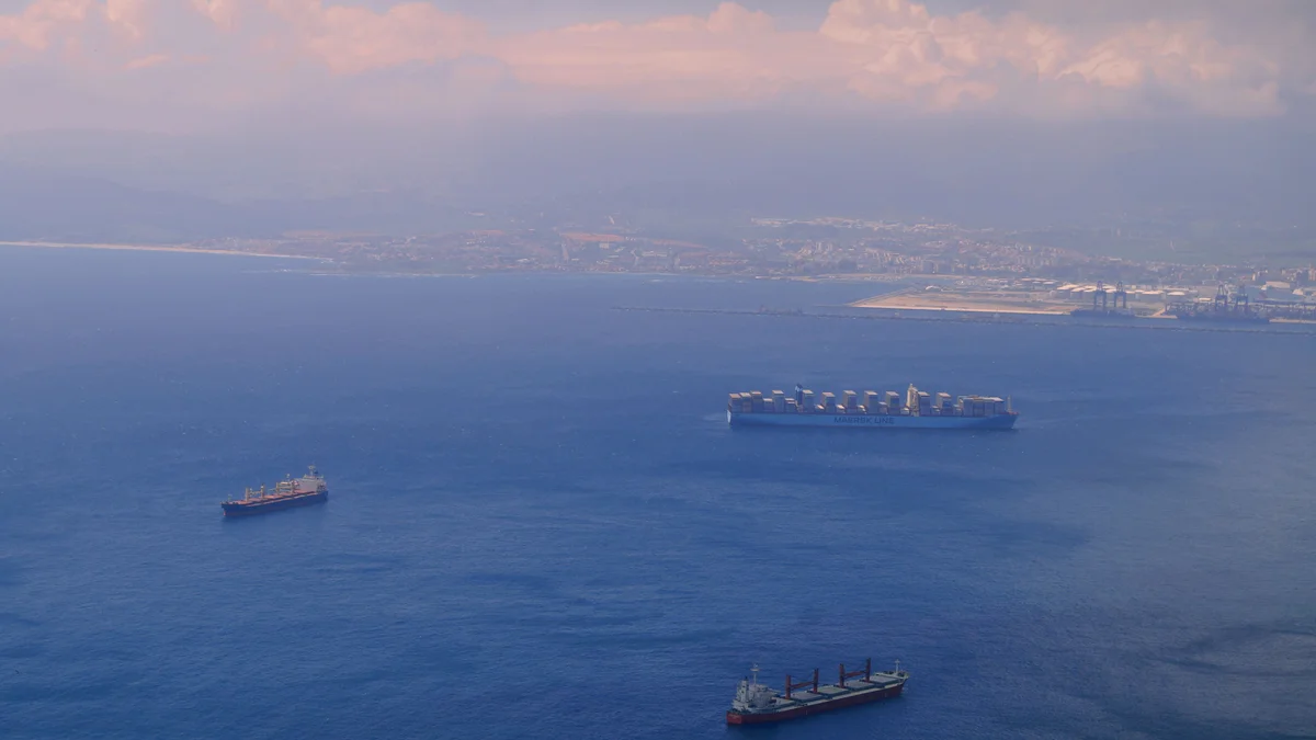 Vista aérea de navios de carga navegando por um estreito entre duas costas, ilustrando o tráfego marítimo em pontos de passagem estratégicos como o Estreito de Ormuz